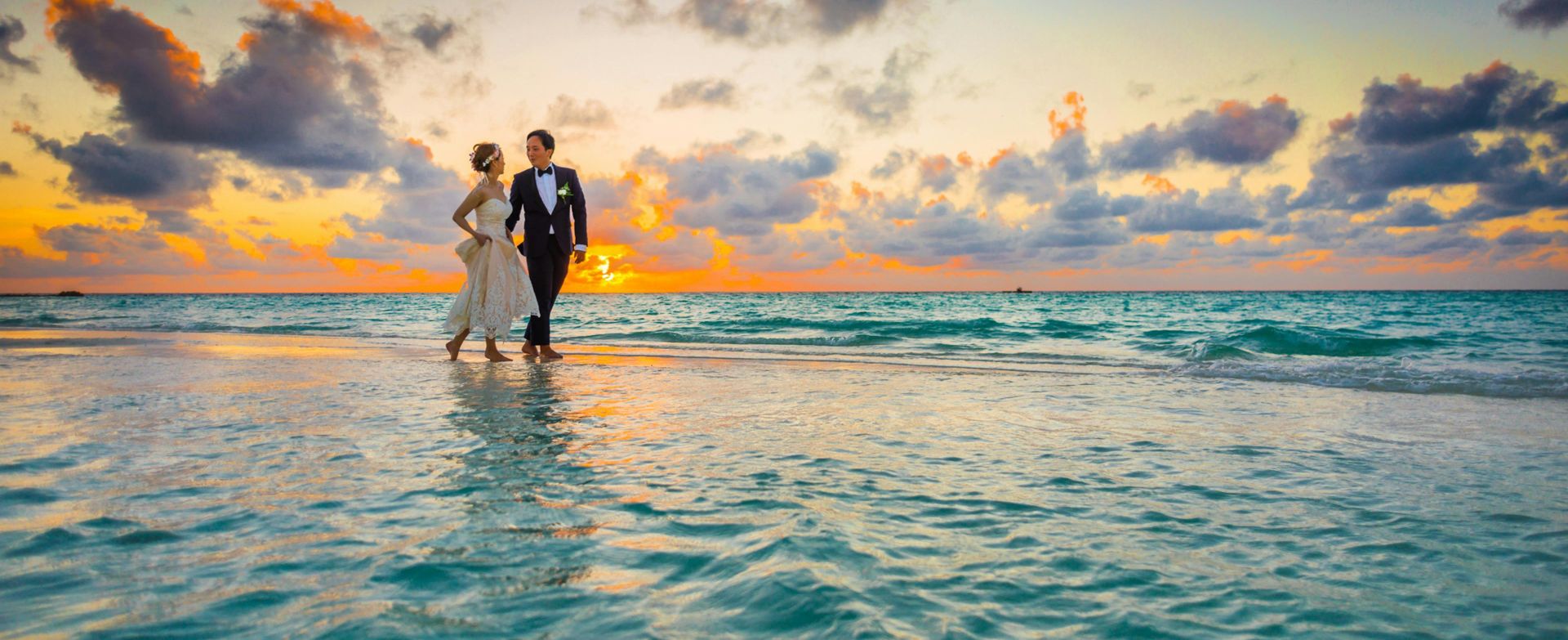 A young couple enjoying a romantic beach wedding during a vibrant sunset.