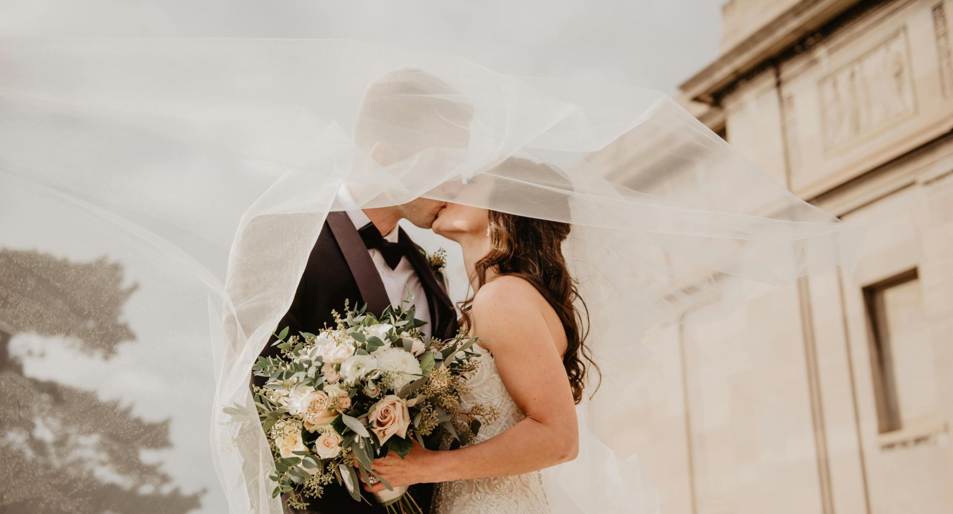 Bride and groom share a tender kiss under a veil, showcasing love and romance on their special day.