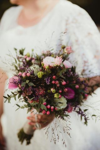 Close-up of a vibrant bridal bouquet held by a woman, showcasing a mix of colorful flowers.