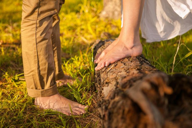 Close-up of a couple's bare feet standing on a log in a sunlit park during fall.
